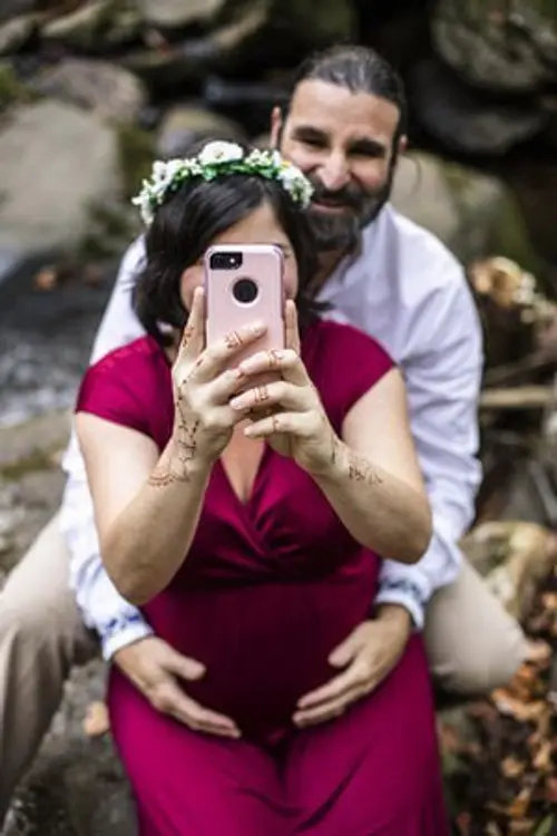 Photo of Phoenix Be behind a pregnant woman taking a mirror selfie outdoors